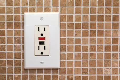 white GFCI outlet on brown tile wall