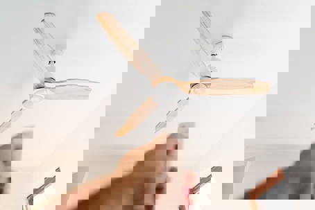 A hand points a remote control at a modern ceiling fan