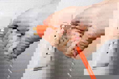 A hand plugs an orange electrical cord